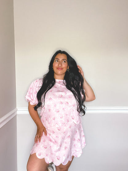 Woman wearing a pink floral set against a plain wall