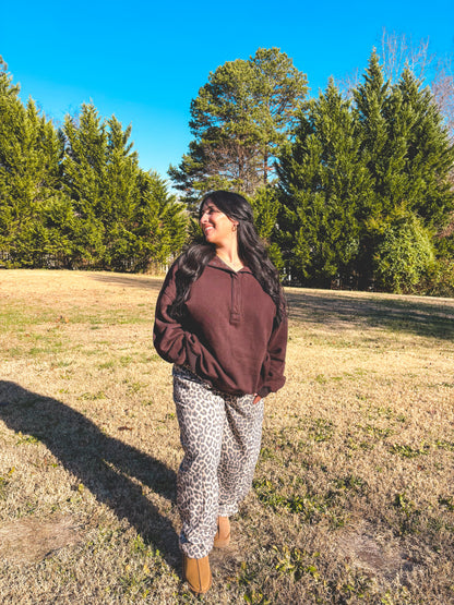 Woman in brown pullover and leopard print pants standing outdoors in sunny weather.
