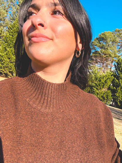 Woman wearing a brown sweater with trees and blue sky in the background