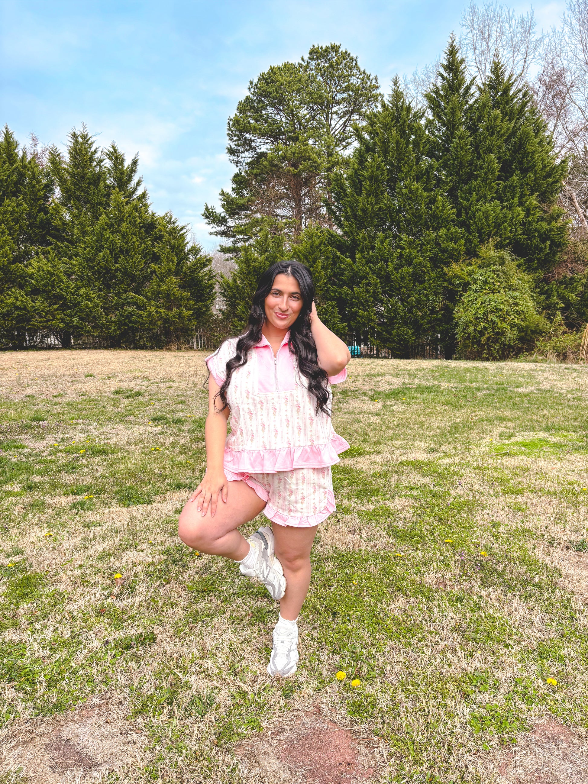 Woman posing in a field with trees in the background