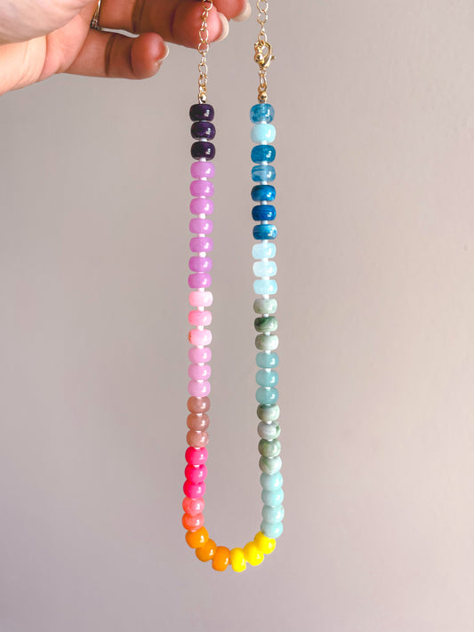 Colorful beaded necklace held by a hand against a plain background