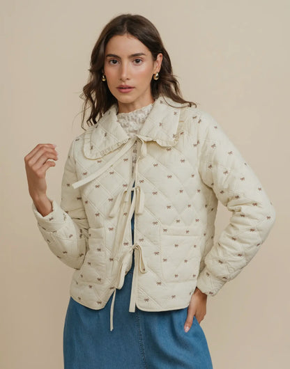 Woman wearing a cream quilted jacket with a subtle bow pattern on a beige background