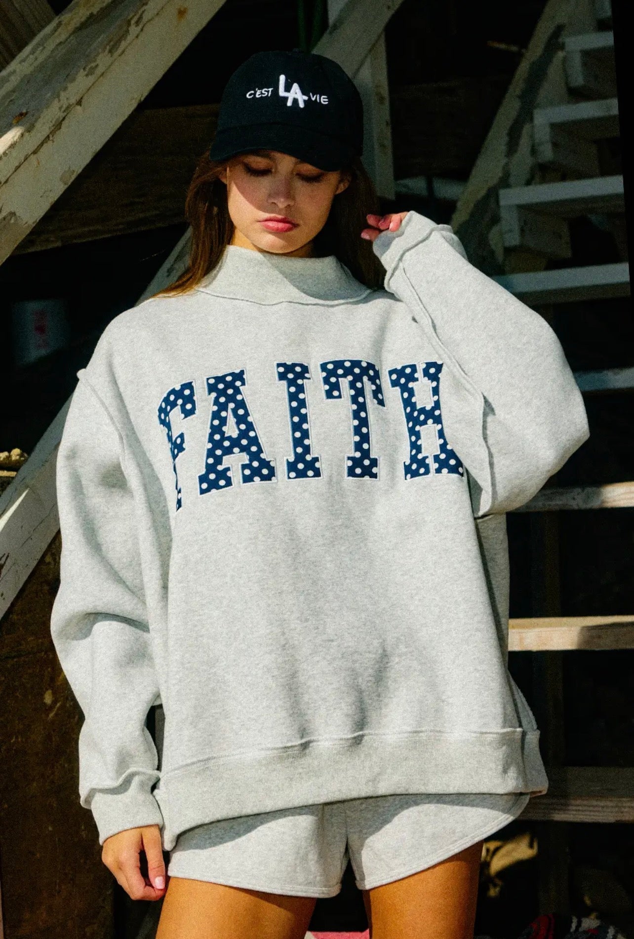 Person wearing a gray sweatshirt with 'FAITH' printed on it, standing outdoors.