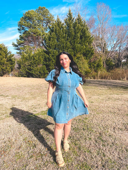 Woman in a denim dress standing in a field with trees in the background