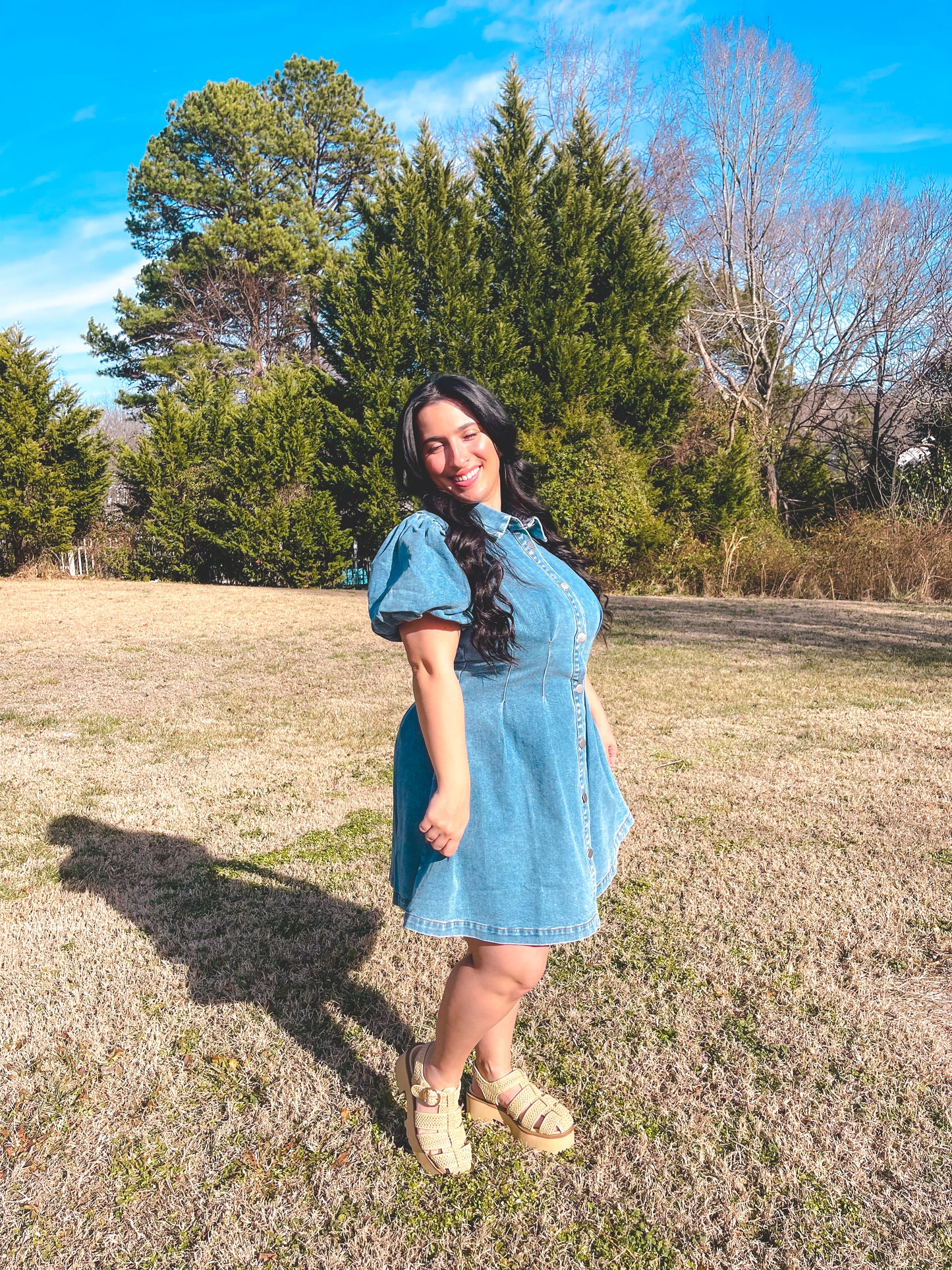 Woman in a blue dress standing in a field with trees in the background