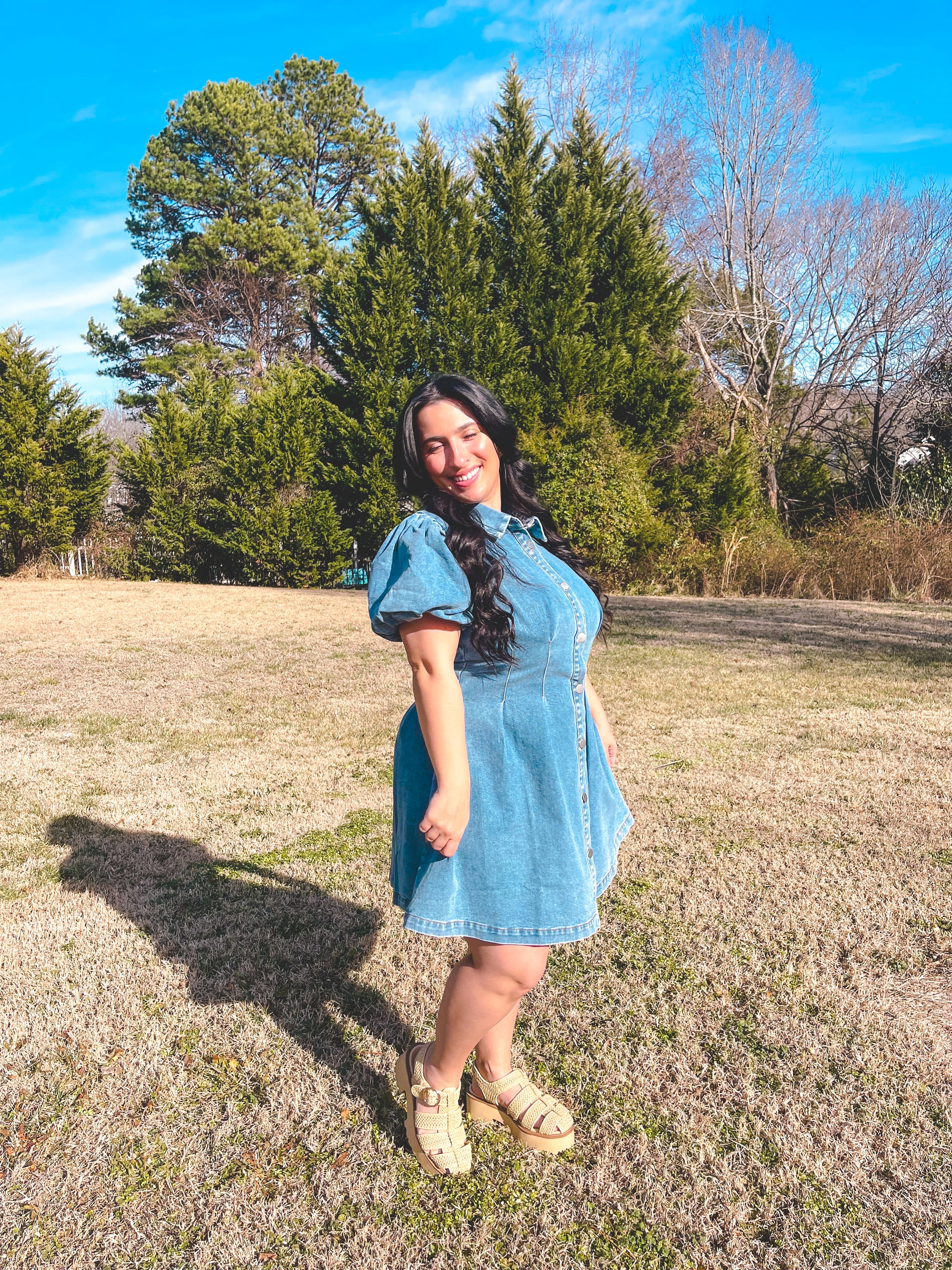 Woman in a blue dress standing in a field with trees in the background