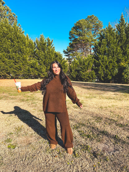 Person in a brown outfit pant set standing in a field with trees in the background