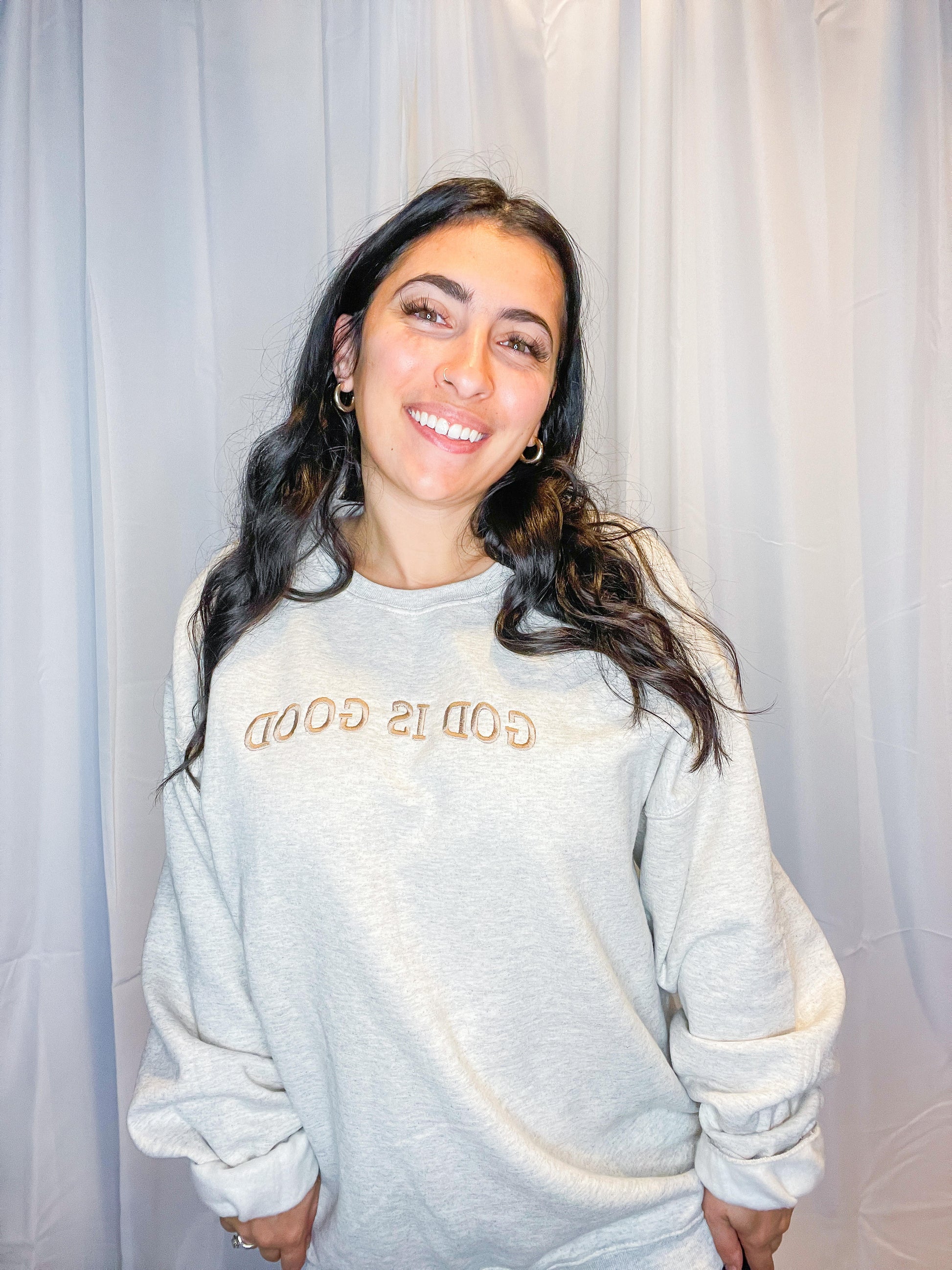 A soft and comfy light grey crewneck sweatshirt with God is Good embroidered on the front.
